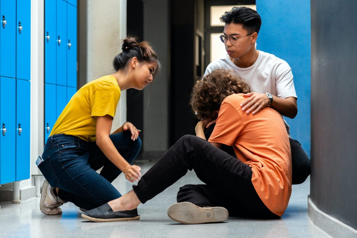 Two teen asian high school students comfort sad classmate victim of bullying in corridor.