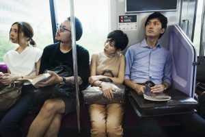 Four people sitting sidy by side on a subway train, Tokyo commuters.